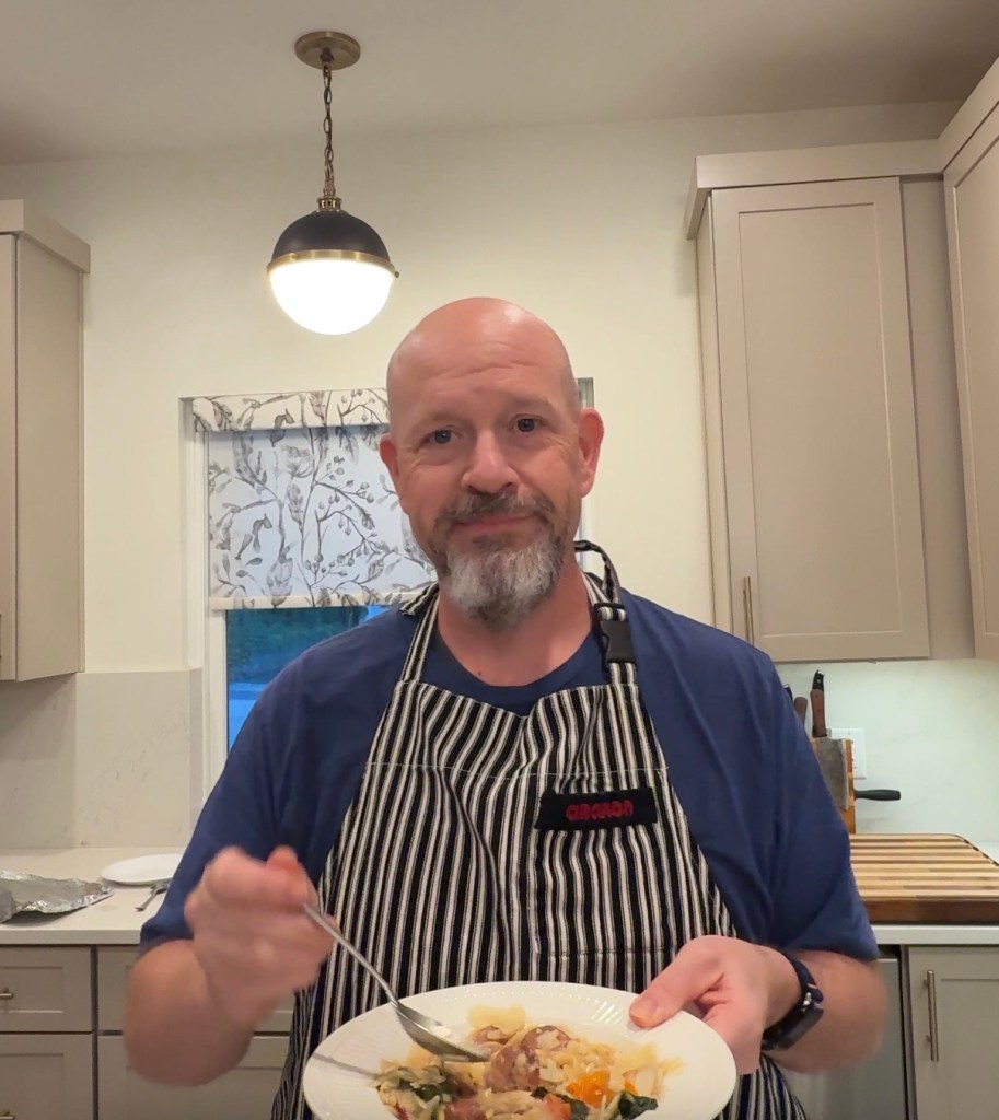 Dwayne in his kitchen in a striped apron, holding a plate of food